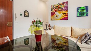 A room with a wooden door, a glass table with a red vase, a sofa with striped pillows, and two abstract paintings on the wall.