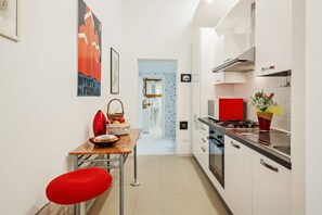A modern kitchen with white cabinets, a red countertop, and a dining area with a red chair and table. - GuestHost - NEW!Palazzo dei Diamanti! Pets Friendly (Ferrara)