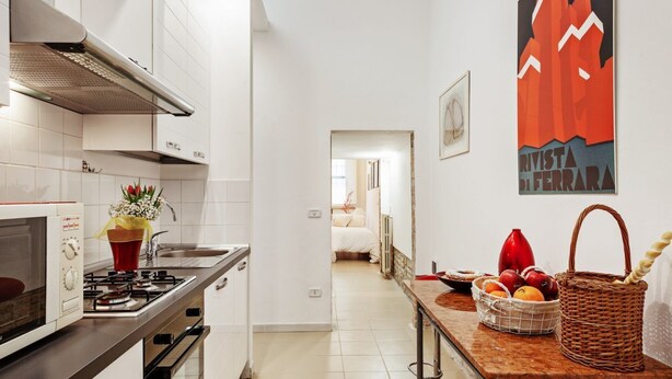 A narrow kitchen with white cabinets, a gas stove, and a red vase with flowers.
