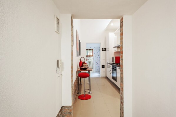 A narrow hallway leading to a kitchen with a red stool and a dining area in the background. - GuestHost - NEW!Palazzo dei Diamanti! Pets Friendly (Ferrara)