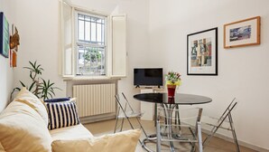 A living room with a sofa, a dining table with chairs, a TV, and artwork on the walls.