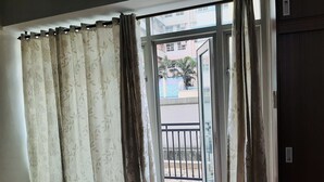 A room with a large window, a curtain, and a view of a building outside. - Modern - Studio Unit Near NAIA3 (Pasay)