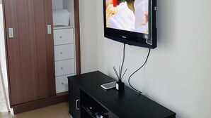 A modern room with a black entertainment unit, a flat-screen TV mounted on the wall, a wooden wardrobe, and a white bedside table. - Modern - Studio Unit Near NAIA3 (Pasay)
