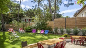 En terrasse med et træbord og røde stole, omgivet af et træhegn og grønne planter.