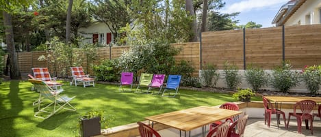 A patio with a wooden table and red chairs, surrounded by a wooden fence and greenery.