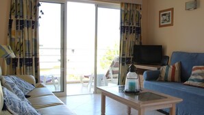 Un salon avec un canapé, une table basse, un téléviseur et un balcon agrémenté de rideaux.
