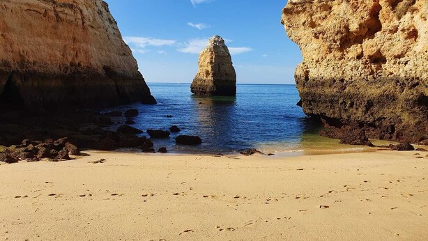 Une plage avec une formation rocheuse imposante au centre, entourée de falaises.