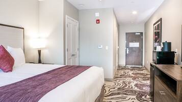 A hotel room with a large bed, a bedside lamp, a wooden dresser, and a patterned carpet.