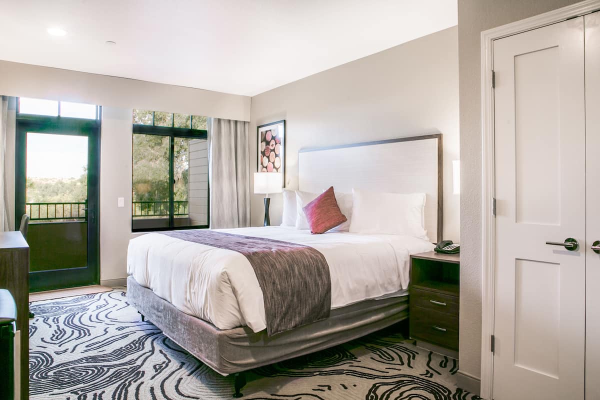 Une chambre d’hôtel avec un grand lit, une table de chevet, une commode et une porte.