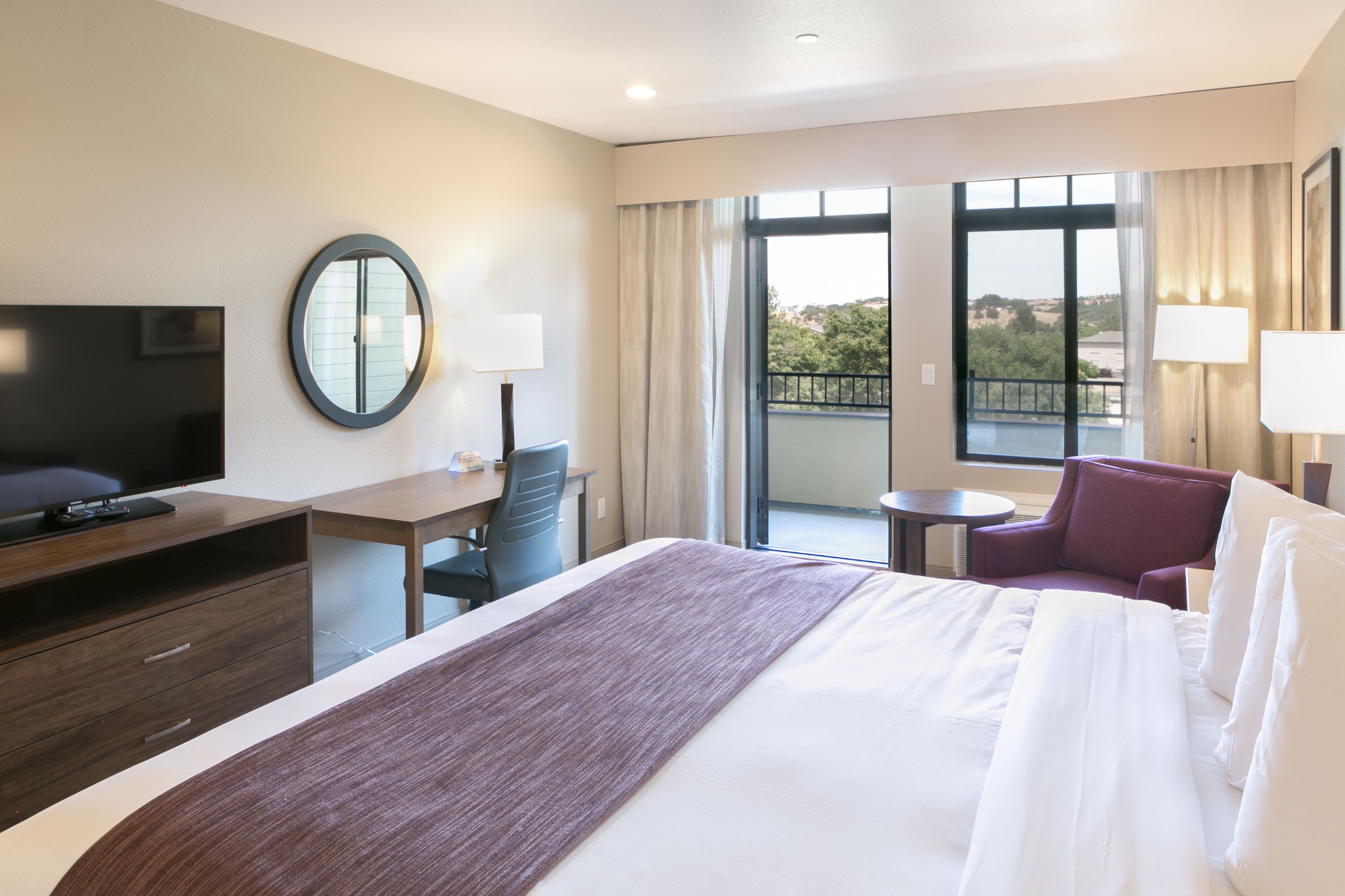 Quarto de hotel com uma cama grande, escrivaninha, cadeira, televisão e varanda com vista.
