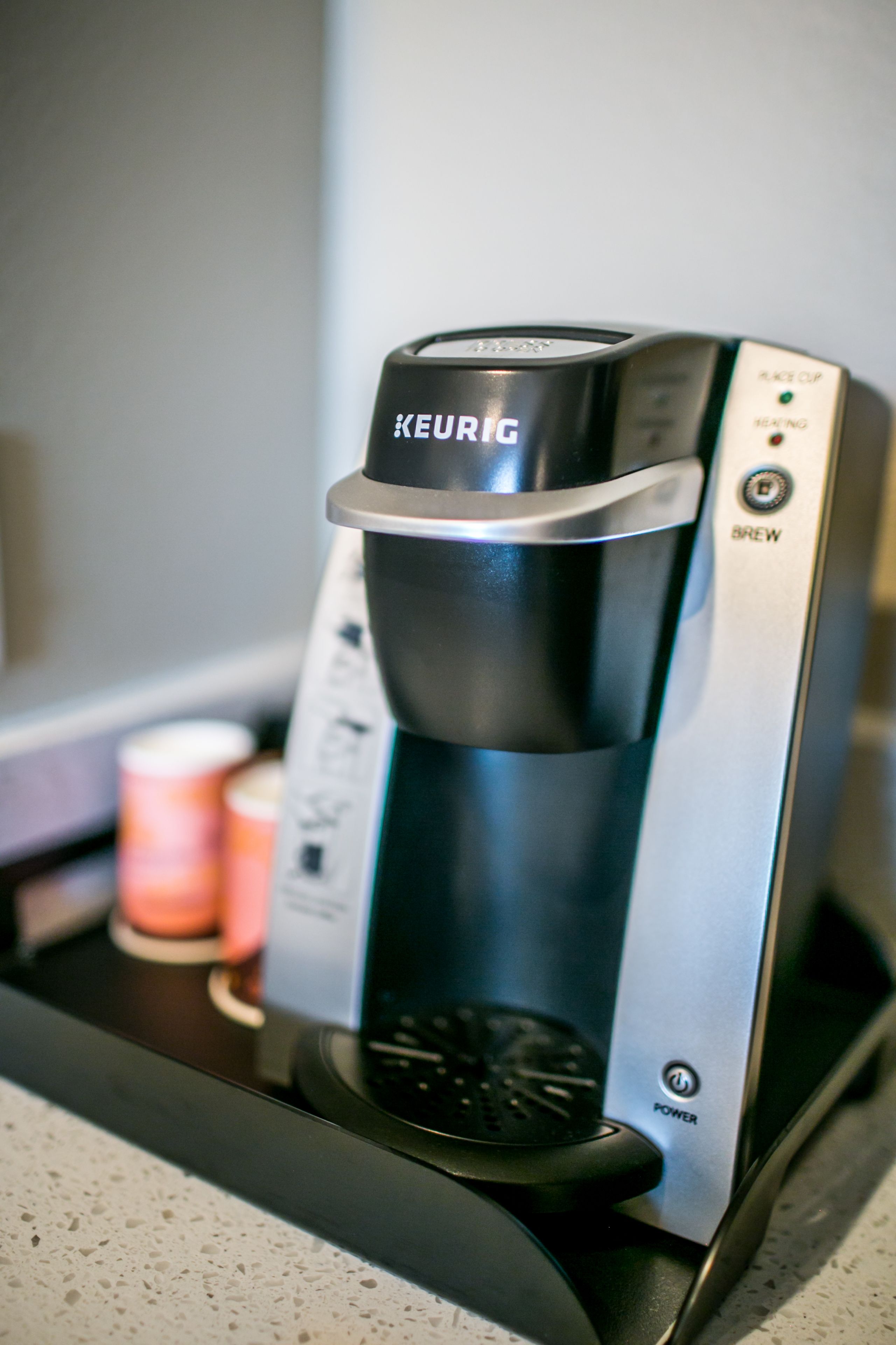Une machine à café Keurig posée sur un plan de travail, avec une dosette de café et une tasse à proximité.