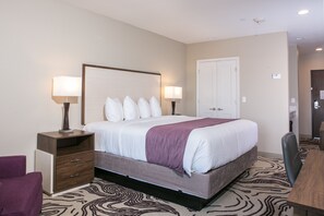 Une chambre d’hôtel avec un grand lit, deux tables de chevet avec des lampes, une chaise et une porte.