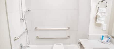 Un baño con una bañera blanca, ducha con cabezal de ducha manual, barra de apoyo y toallero.