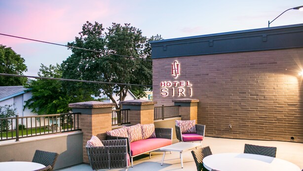 Un espacio al aire libre con sofá y sillones, una mesa y un muro de ladrillo con un letrero de neón que dice "HOTEL SIRI".