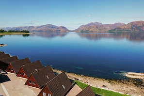 A lakeside view with red-roofed houses and mountains in the background.