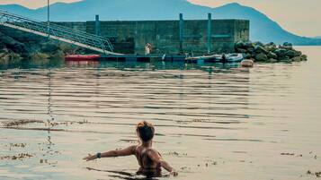 Una persona en el agua, con un muelle y barcos al fondo.