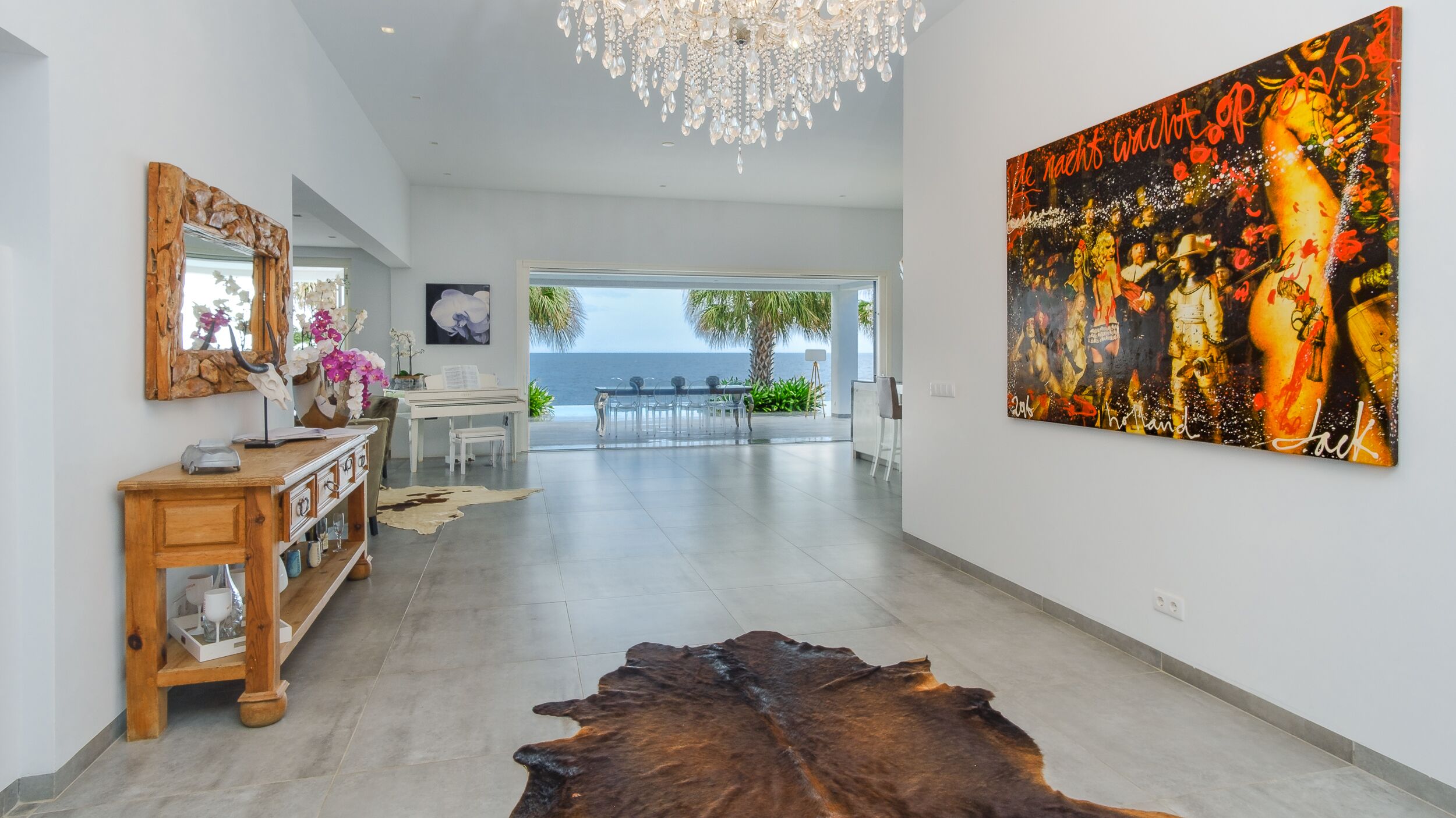 A spacious hallway with a piano, a large painting, and a view of the ocean.