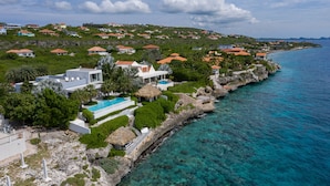 Une propriété située sur la côte, dotée d’une piscine, d’une végétation luxuriante et d’un rivage rocheux.