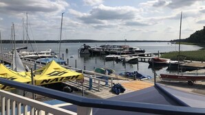 A marina with various boats docked, a yellow tent with 'NAISH' branding, and a view of the water and distant shoreline. - Time by the Lake. Wildrose Duplex – Fireplace, Loggia, View of the Greenery (Bad Saarow)