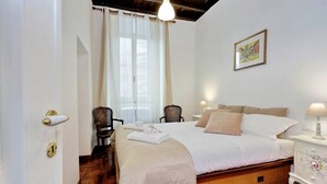 Um quarto com uma cama, uma cadeira, uma mesa de cabeceira com abajur, uma porta com olho de fechadura e uma janela com cortinas.