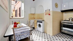 Cozinha compacta com máquina de lavar, forno e área de refeições com mesa e cadeiras.