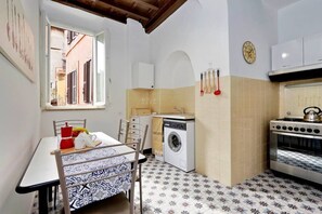 A compact kitchen with a washing machine, oven, and dining area with a table and chairs.