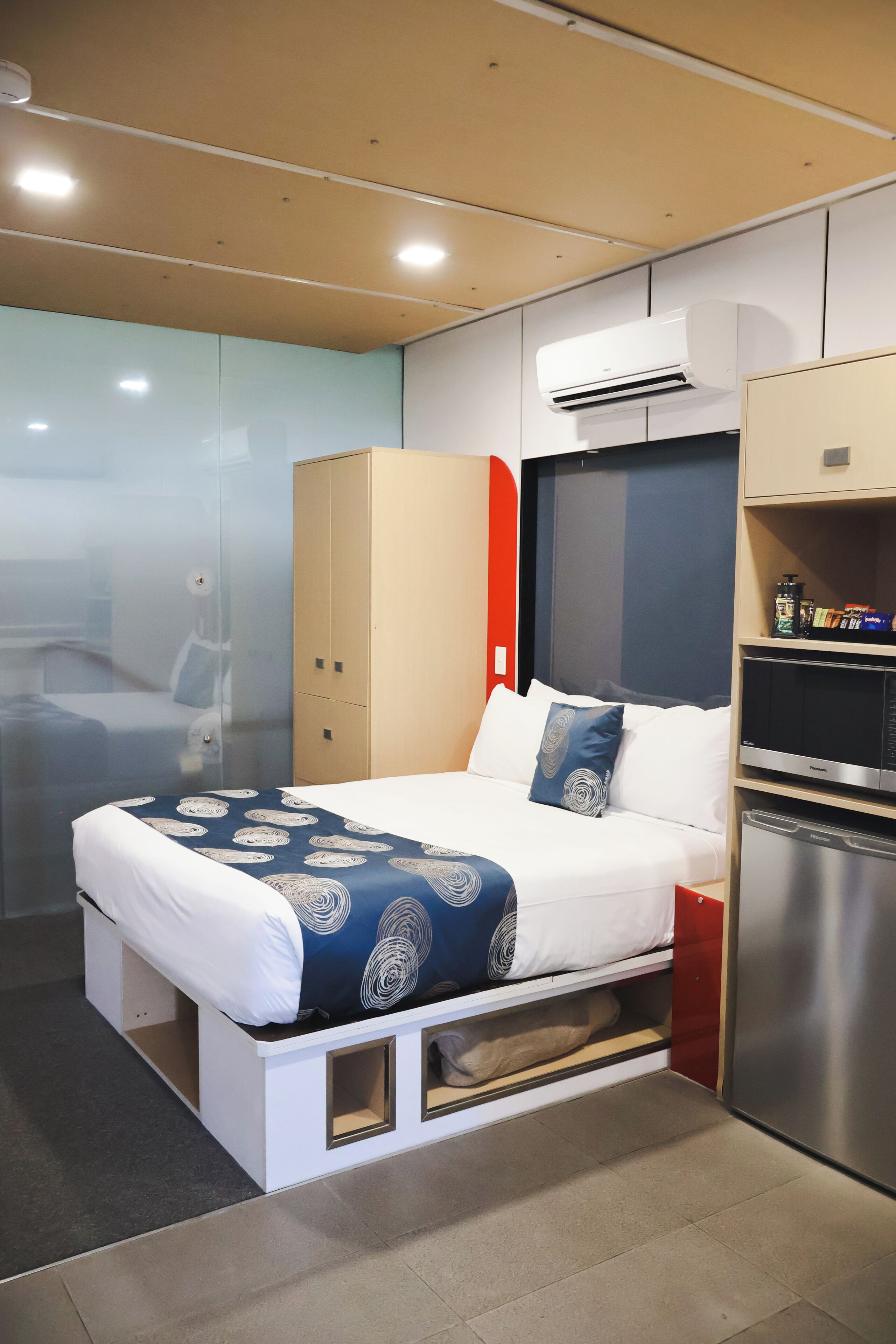 A modern hotel room with a bed, wardrobe, and built-in air conditioning unit.