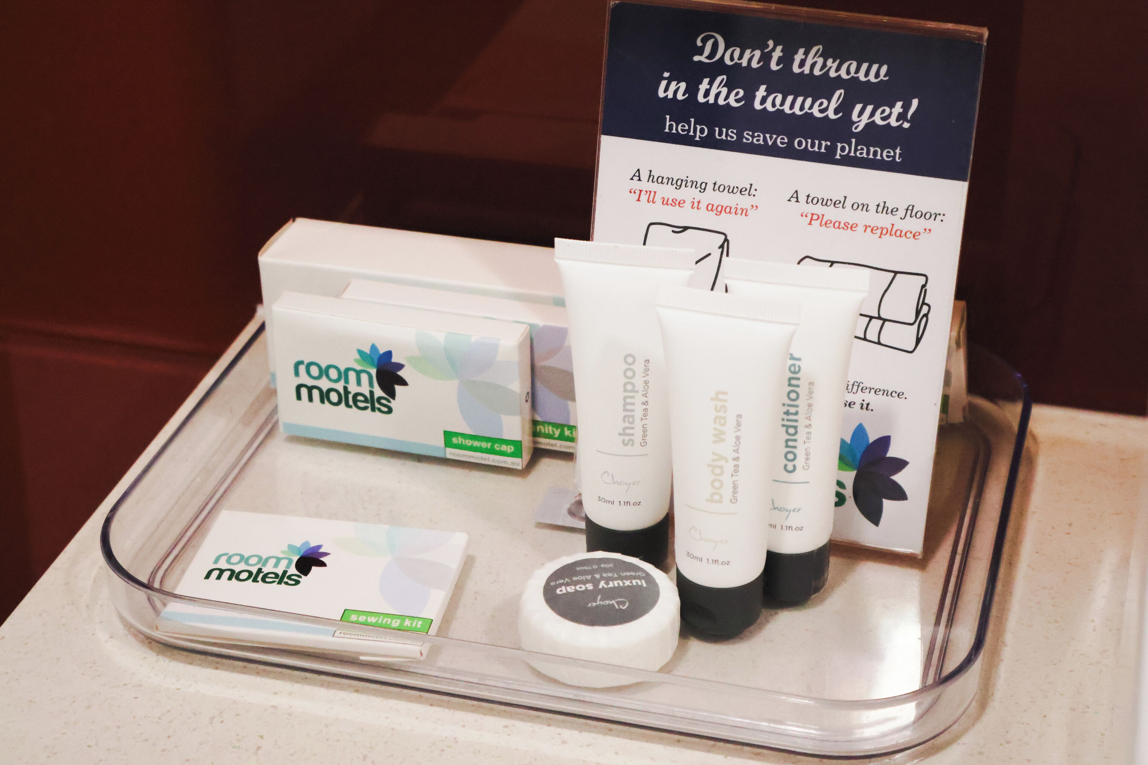 Un plateau de bienvenue dans une chambre d’hôtel, contenant des articles de toilette, un bonnet de douche et un panneau indiquant les consignes d’utilisation des serviettes.