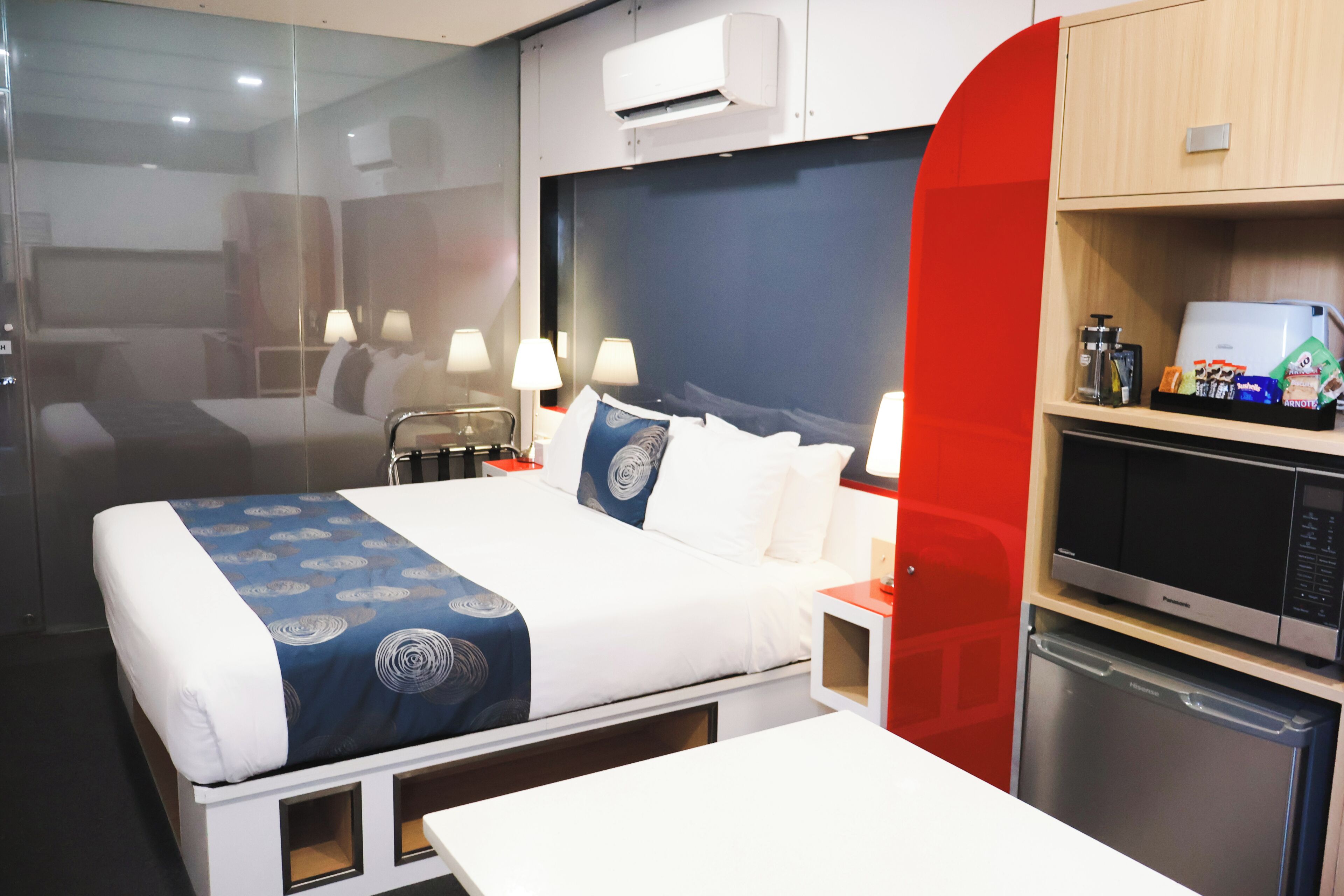 Ein Hotelzimmer mit Bett, Nachttischlampen, einer Minibar und einer Mikrowelle.