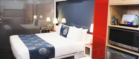 A hotel room with a bed, bedside lamps, a minibar, and a microwave.