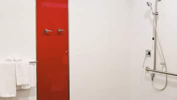 A bathroom with a red door, white tiles, a shower area, and a white chair.