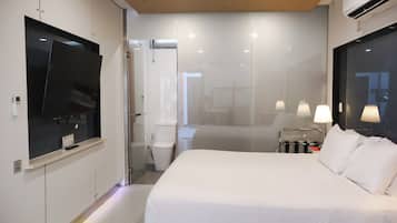 A hotel room with a bed, a TV, a bathroom, and a window.