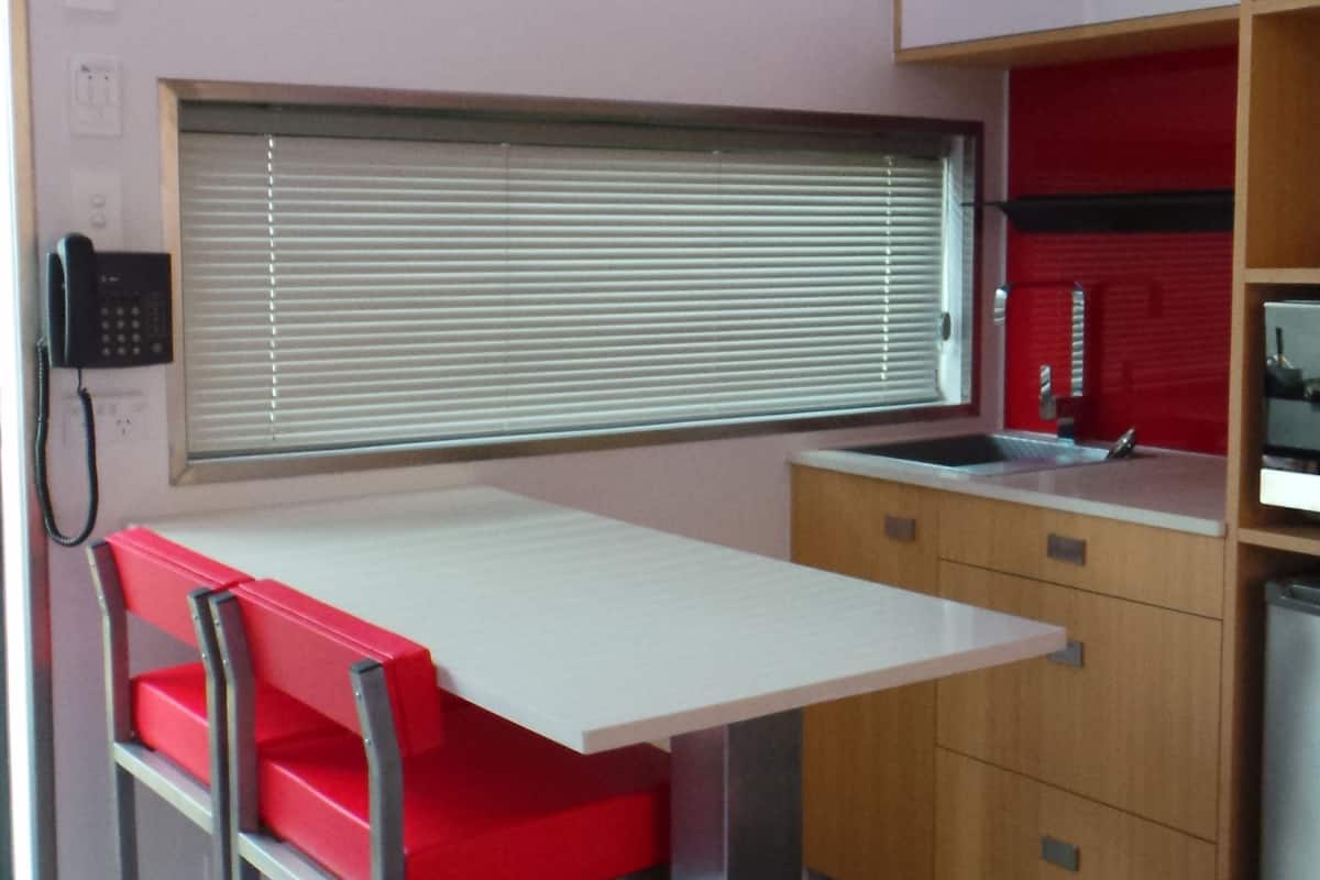 A compact kitchen with a white countertop, a red bench, and wooden cabinets.