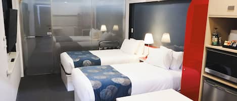 A hotel room with two beds, a desk, a minibar, and a television.