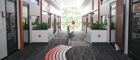 A modern hotel corridor with a curved bench, glass doors, and potted plants.