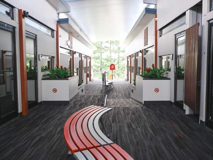 A modern hotel corridor with a curved bench, glass doors, and potted plants.