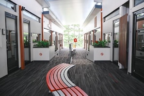 A modern hotel corridor with a curved bench, glass doors, and potted plants. - Stay Motel (Gympie)