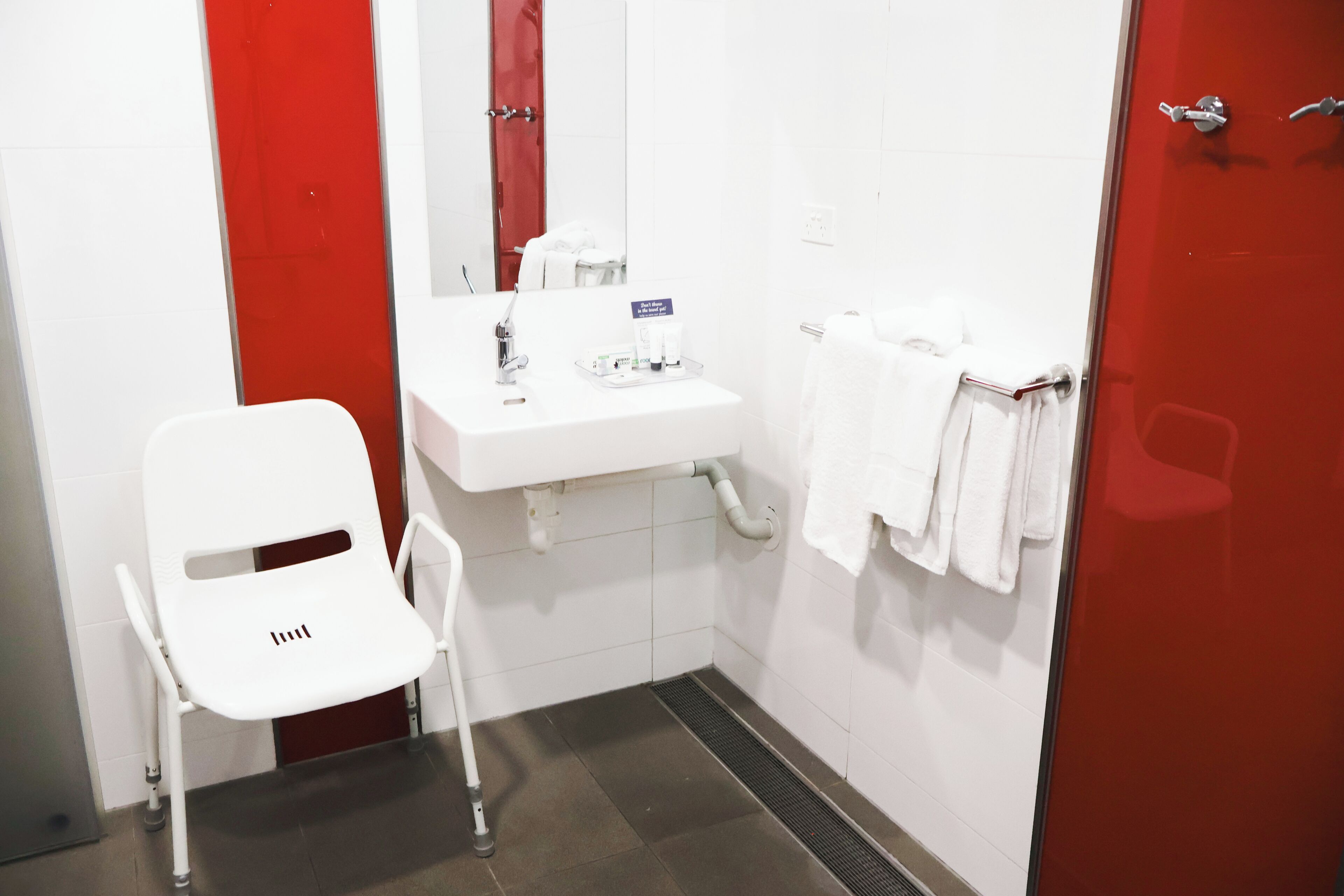 A small, white bathroom with a single white chair, a sink, and a mirror.