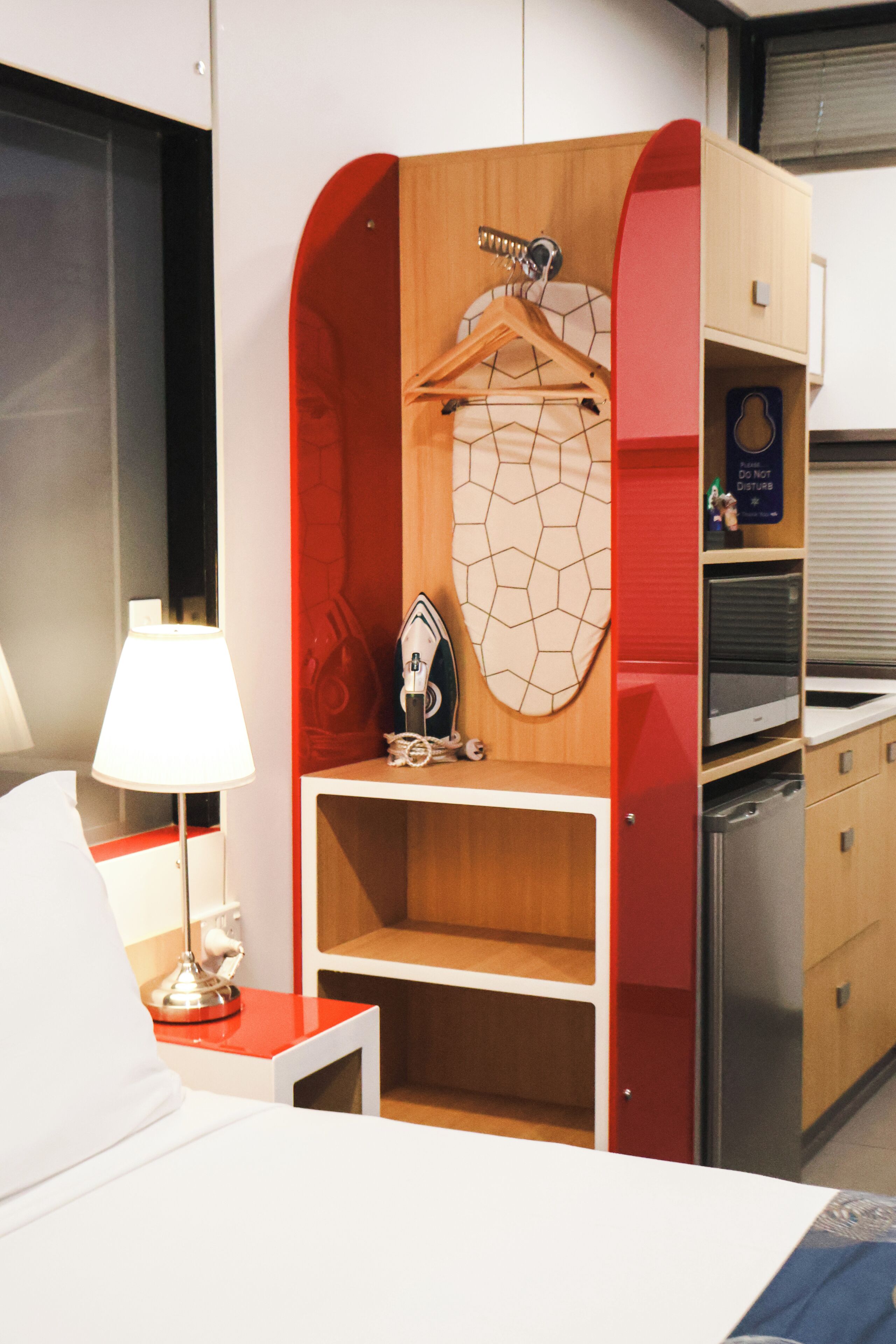 Hotelkamer met een bed, een bureau met lamp, een kledingkast met spiegel en een klein plankje met decoratie.