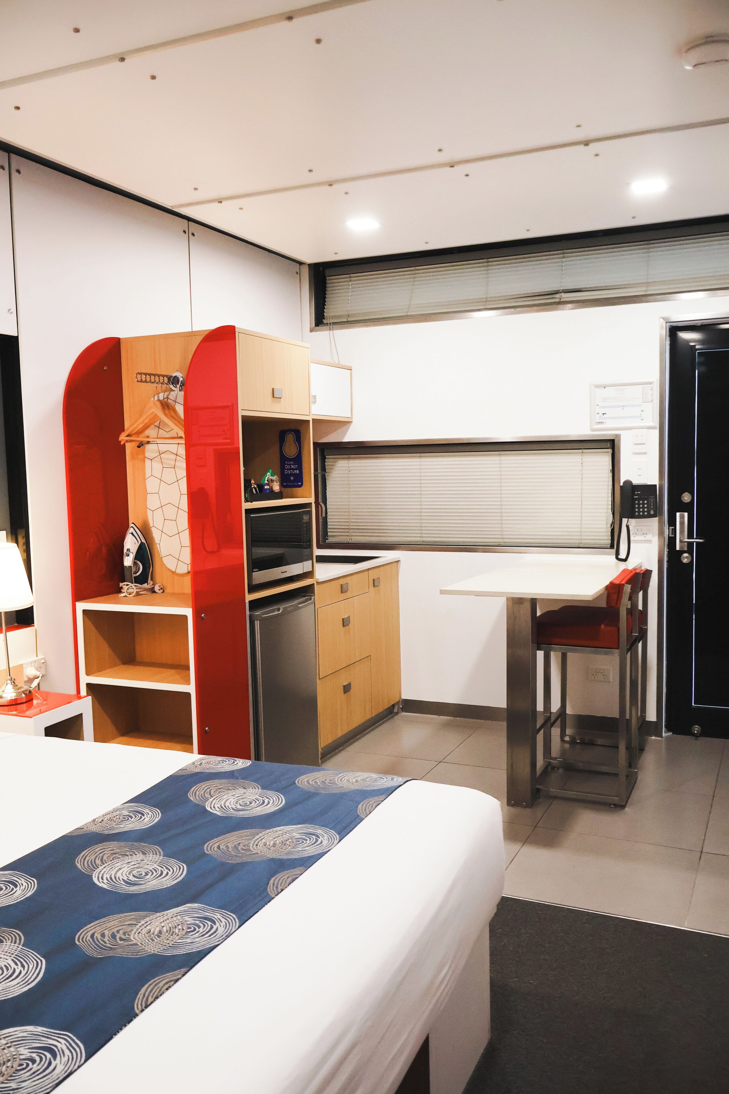 A compact hotel room with a bed, a desk, a kitchenette, and a wardrobe.