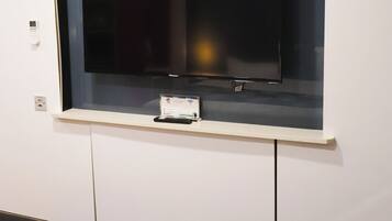 A hotel room with a television mounted on a wall, a bed with a patterned bedspread, and a small table with a remote control.