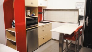Una kitchenette compacta con microondas, horno y un refrigerador pequeño. Incluye una silla y una mesa con teléfono integrado.