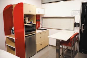 A compact kitchenette with a microwave, oven, and a small refrigerator. There is a single chair and a table with a built-in telephone. - Stay Motel (Gympie)