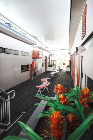 A corridor with a modern design, featuring a central walkway, seating areas, and a fire safety sign. - Stay Motel (Gympie)