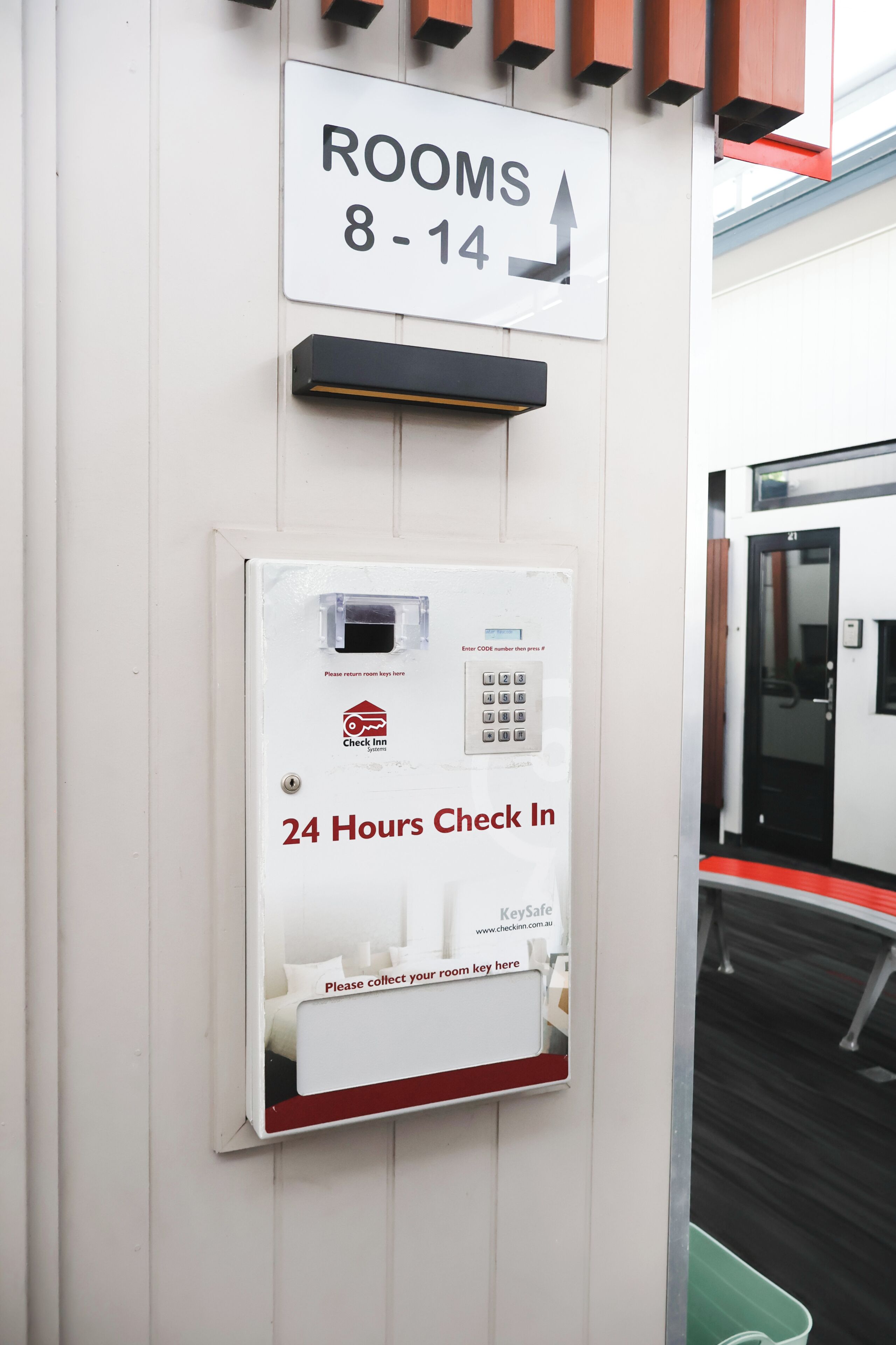 A wall-mounted sign indicating rooms 8-14 with a 24-hour check-in system and a keypad for room key collection.