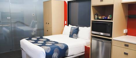A compact hotel room with a bed, a built-in microwave, a mini fridge, and a small kitchenette area.