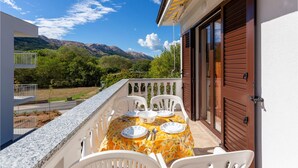 An outdoor dining area with a table set for four, surrounded by white chairs, overlooking a mountainous landscape. - Beach front apartment in Jurandvor (Jurandvor)