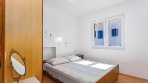 A bedroom with a wooden bed, a bedside table, a mirror, and a window with blinds. - Beach front apartment in Jurandvor (Jurandvor)