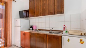 A compact kitchen with wooden cabinets, a built-in microwave, a sink, and a refrigerator. - Beach front apartment in Jurandvor (Jurandvor)