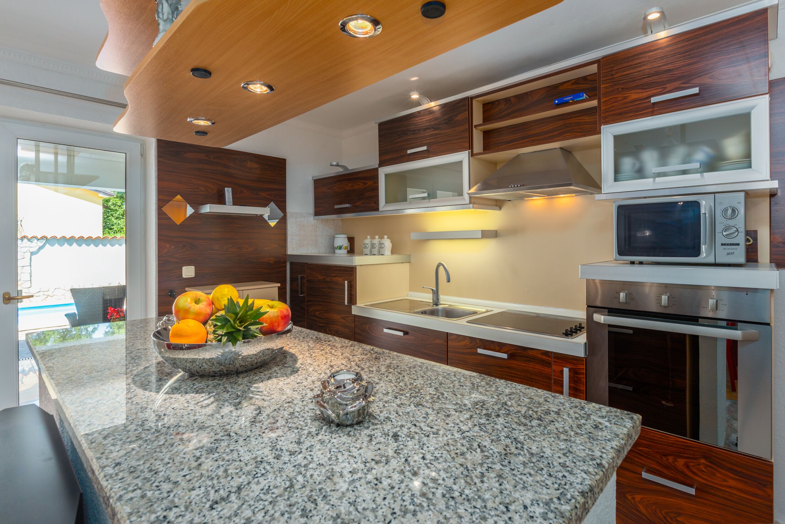 A modern kitchen with granite countertops, wooden cabinets, a built-in microwave, and a stainless steel oven.